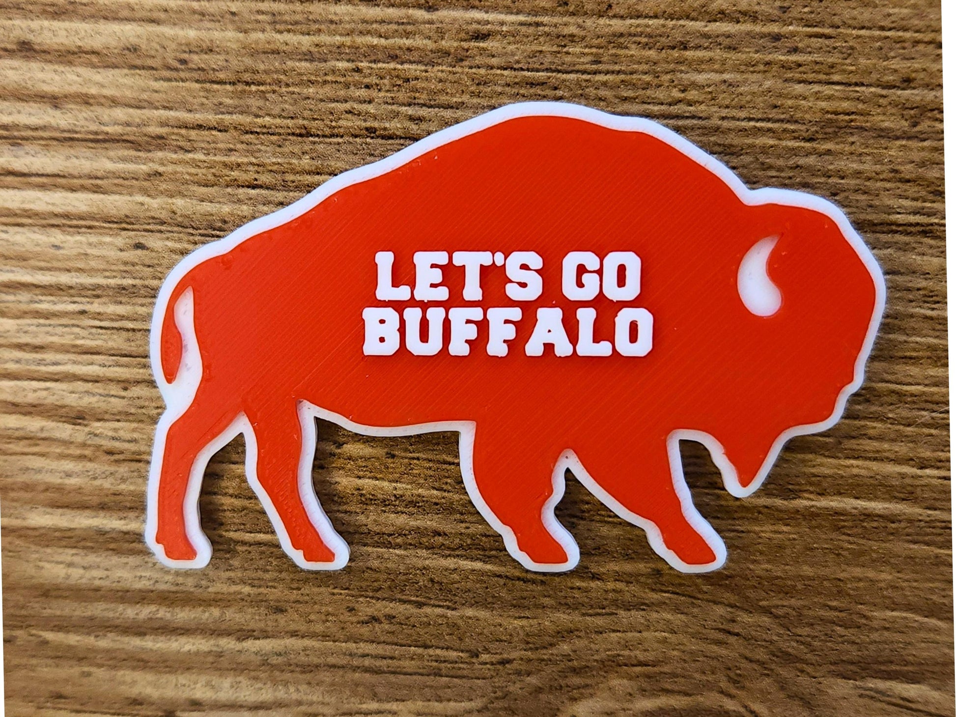 A close up of a single red Lets Go Buffalo magnets stacked on a wooden surface.
