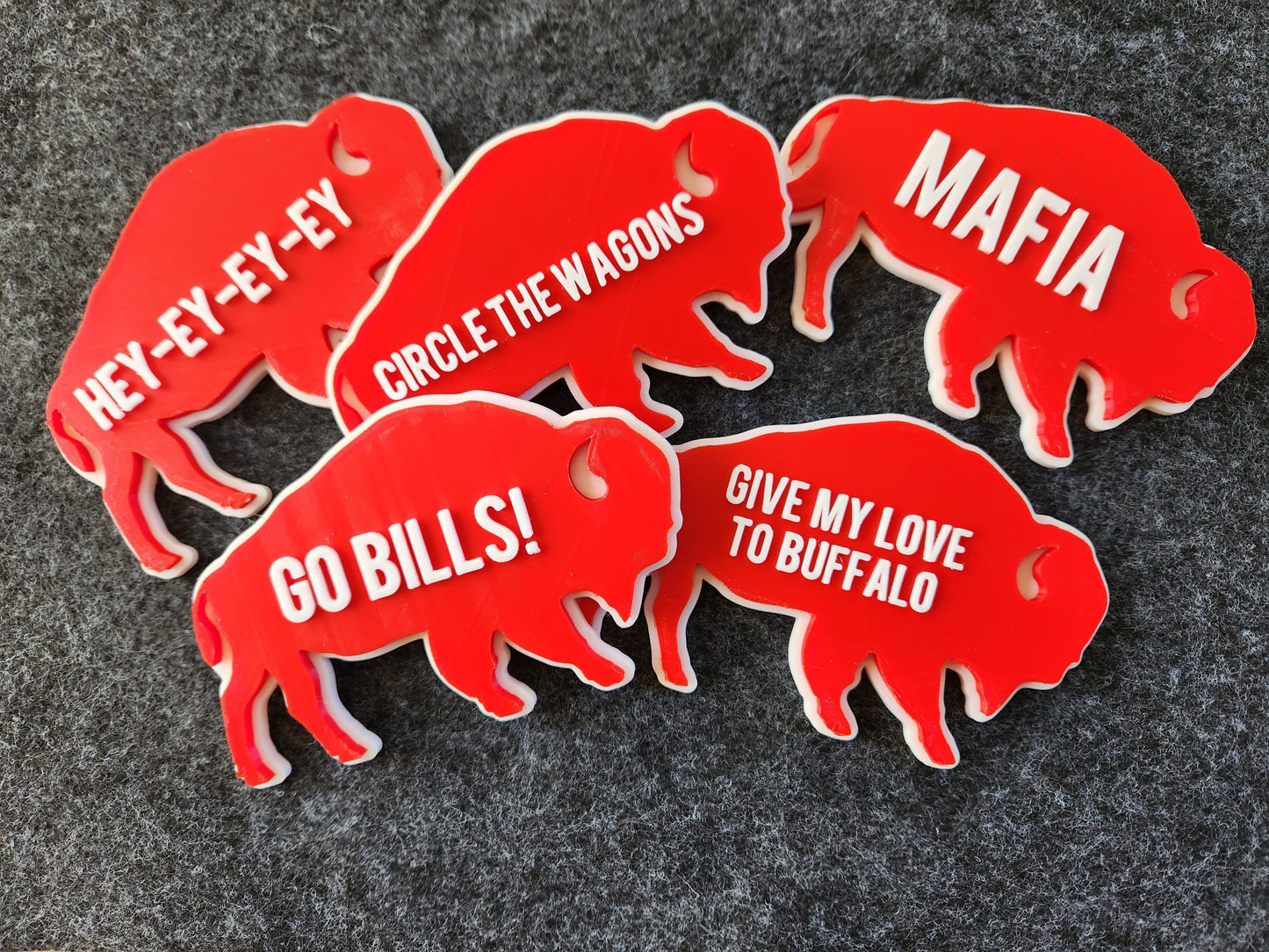 5 Retro style Buffalo Bills magnets pictured on a gray background. They Feature team phrases like Go Bills, MAFIA, Hey-ey-ey-ey and GO BILLS! in raised white letters on a red background.