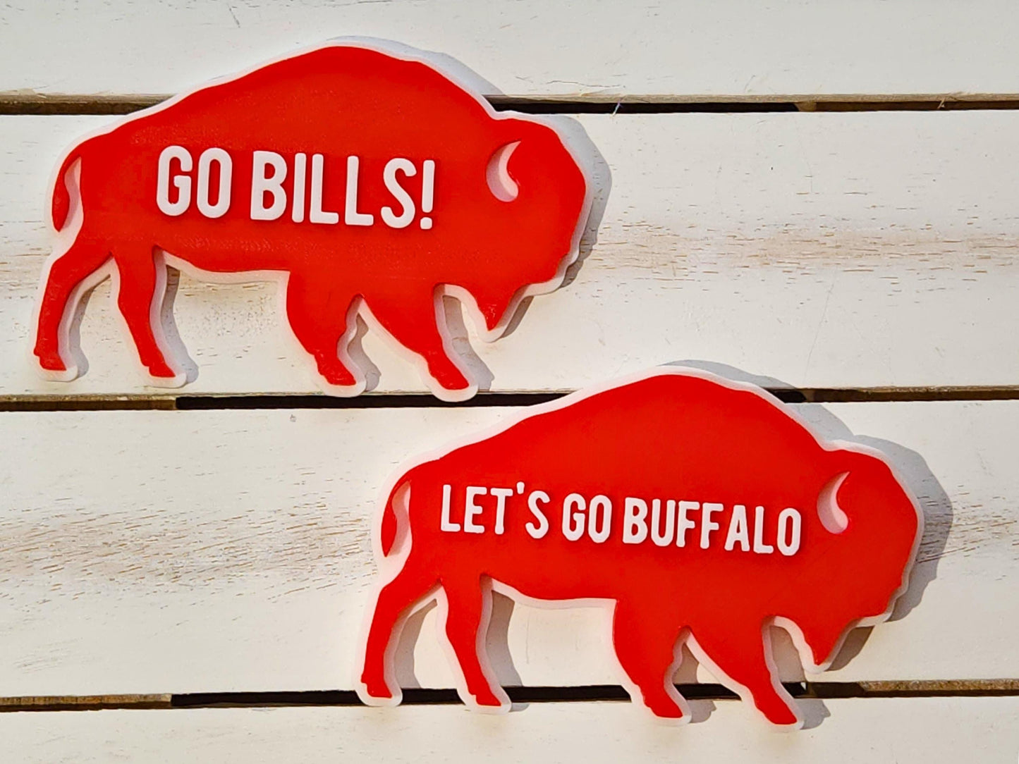 2 Retro Buffalo Bills magnets pictured on a wooden background. One says Let's Go Buffalo and the other says Go Bills in raised white letters on a bright red background.