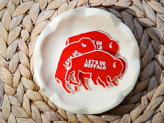 Pile of red Lets Go Buffalo magnets stacked in a white bowl on a woven surface.