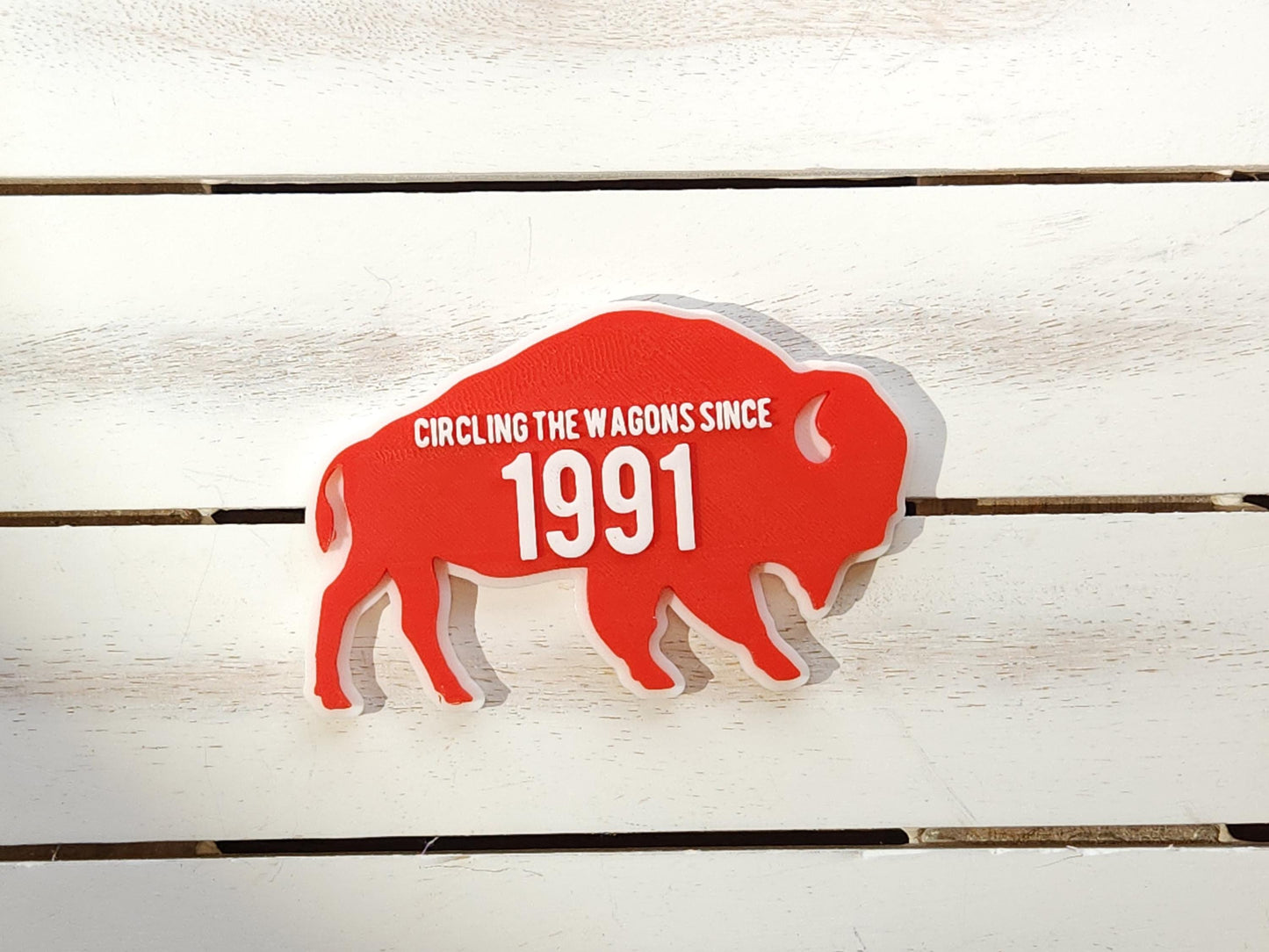 A red magnet for Buffalo Bills fans that says Circling the Wagons since 1991 that can be customized with any year. It is shown on a wooden background.