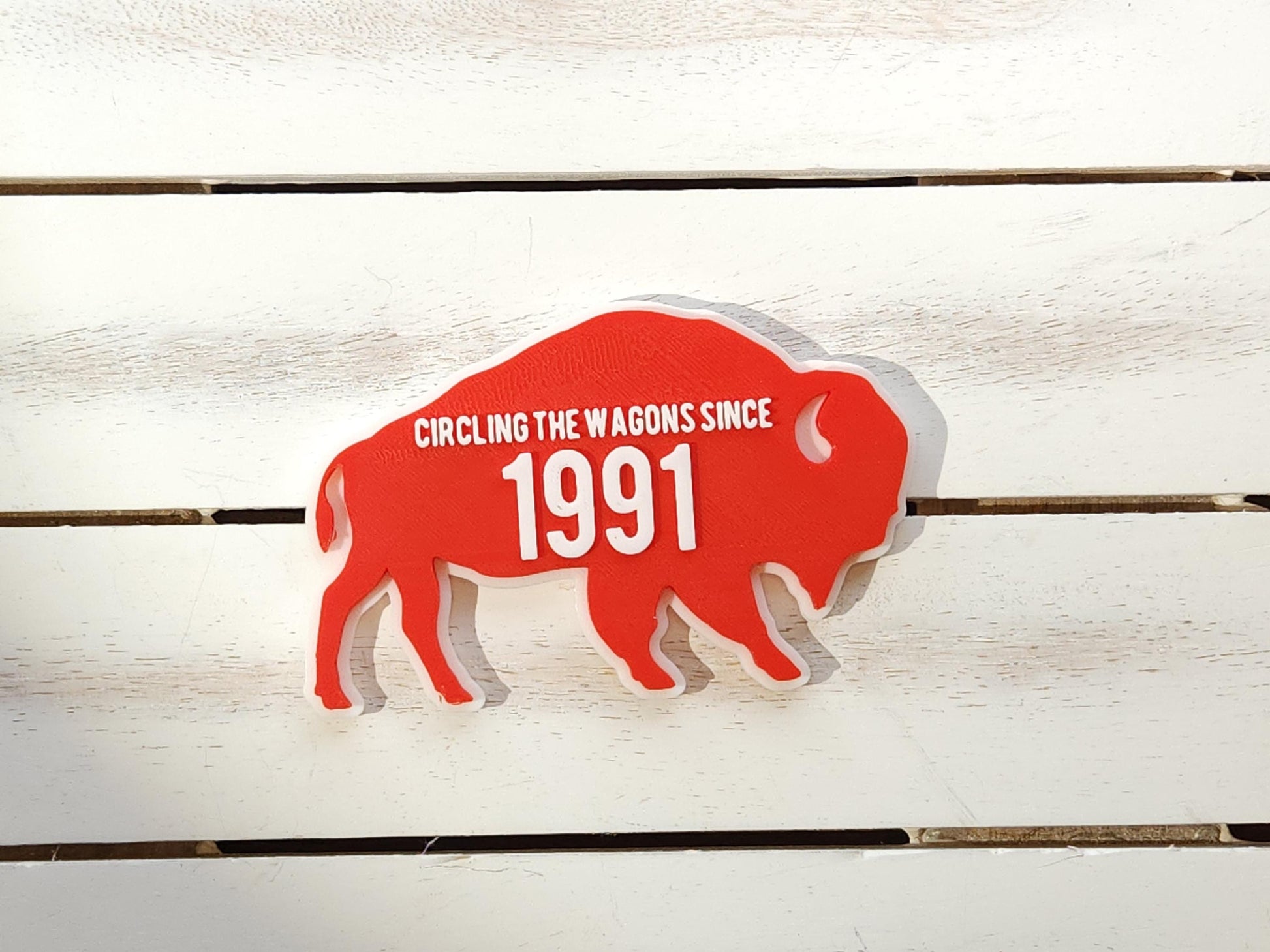 A red magnet for Buffalo Bills fans that says Circling the Wagons since 1991 that can be customized with any year. It is shown on a wooden background.