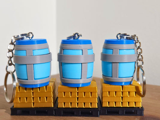 A close up picture of a set of 3 Chug Jug keychains from Fortnite, stacked on top of gold bar toys. The top has a mechanical clicker that can be used for anti-stress or as a fidget toy.