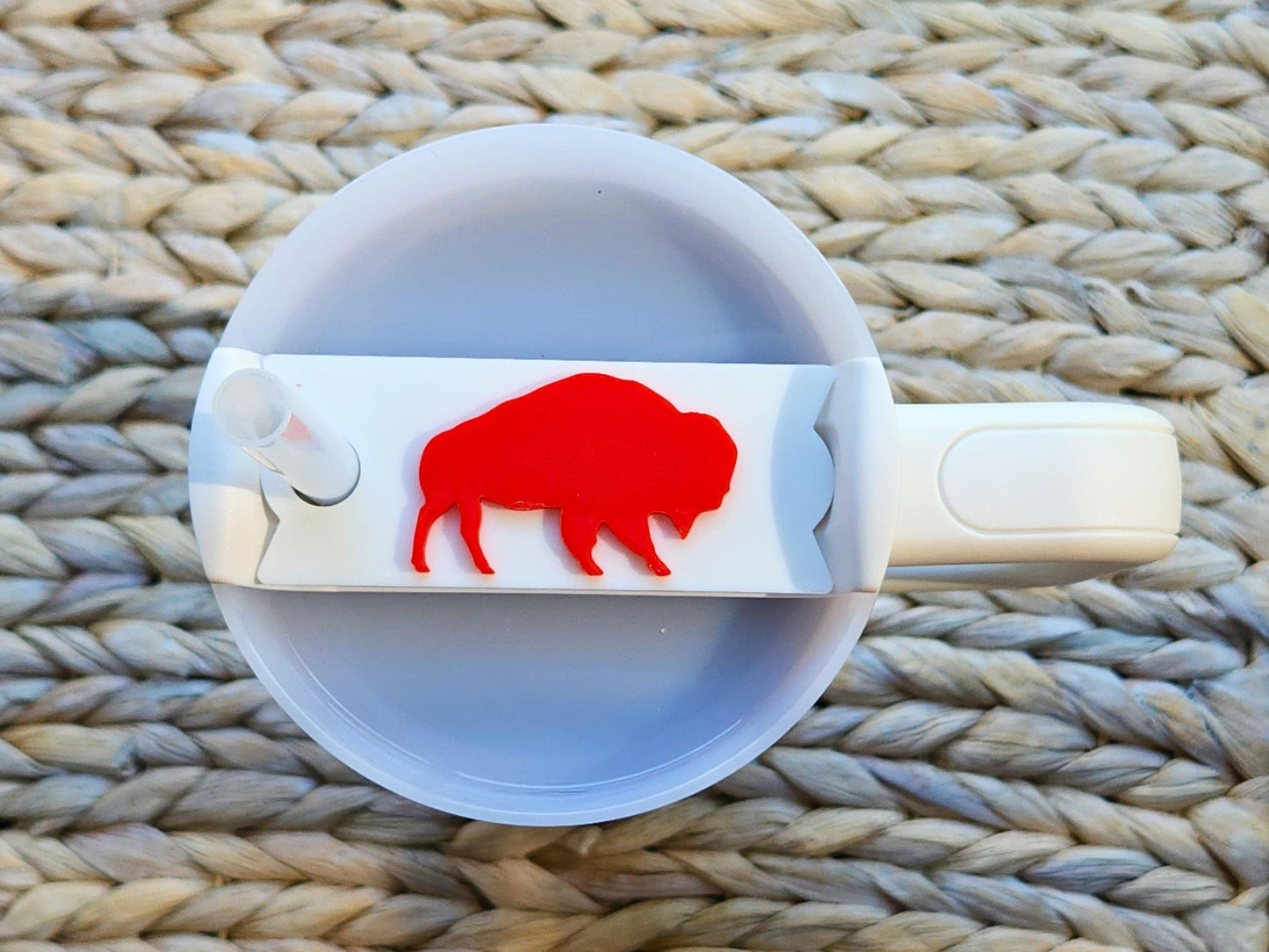 White Stanley tumbler topper featuring a bold red buffalo silhouette, placed on a cream tumbler to showcase a clean, team-inspired design.