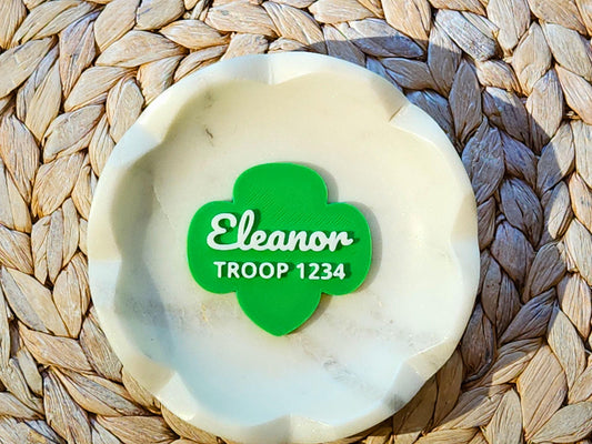 A personalized green Girl Scout-shaped magnet displayed in a white dish. It features the name 'Eleanor' in a white script font and 'TROOP 1234' underneath in bold capital letters.