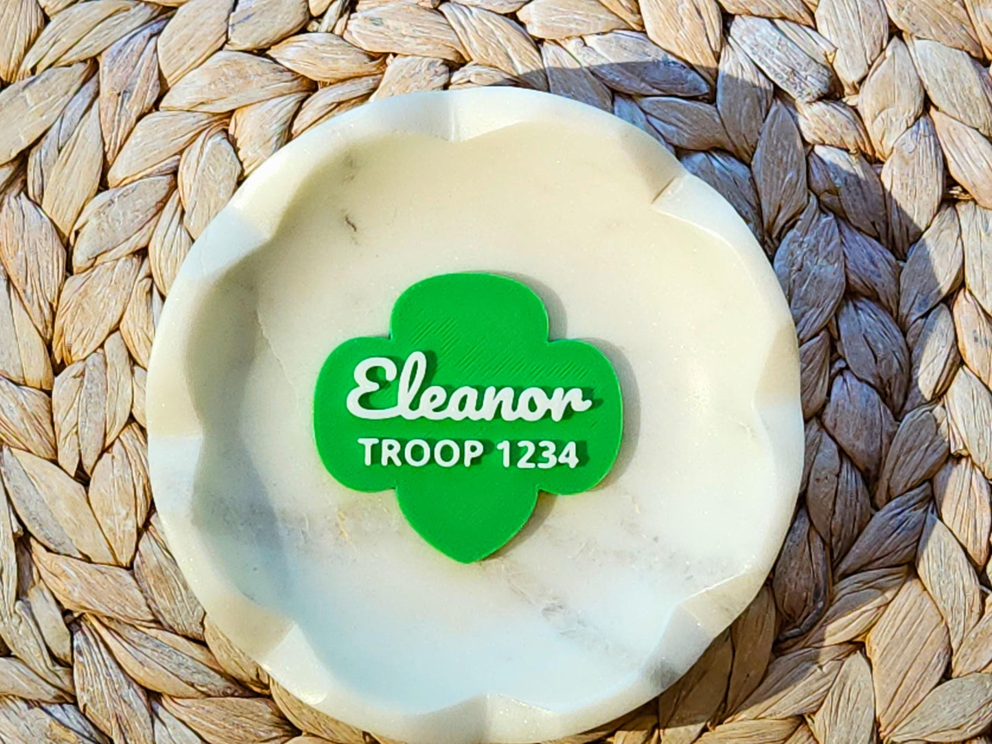 Personalized Girl Scout pin in green trefoil shape with name "Eleanor" and Troop 1234 in white text, displayed in a marble dish—custom gift for Girl Scouts.