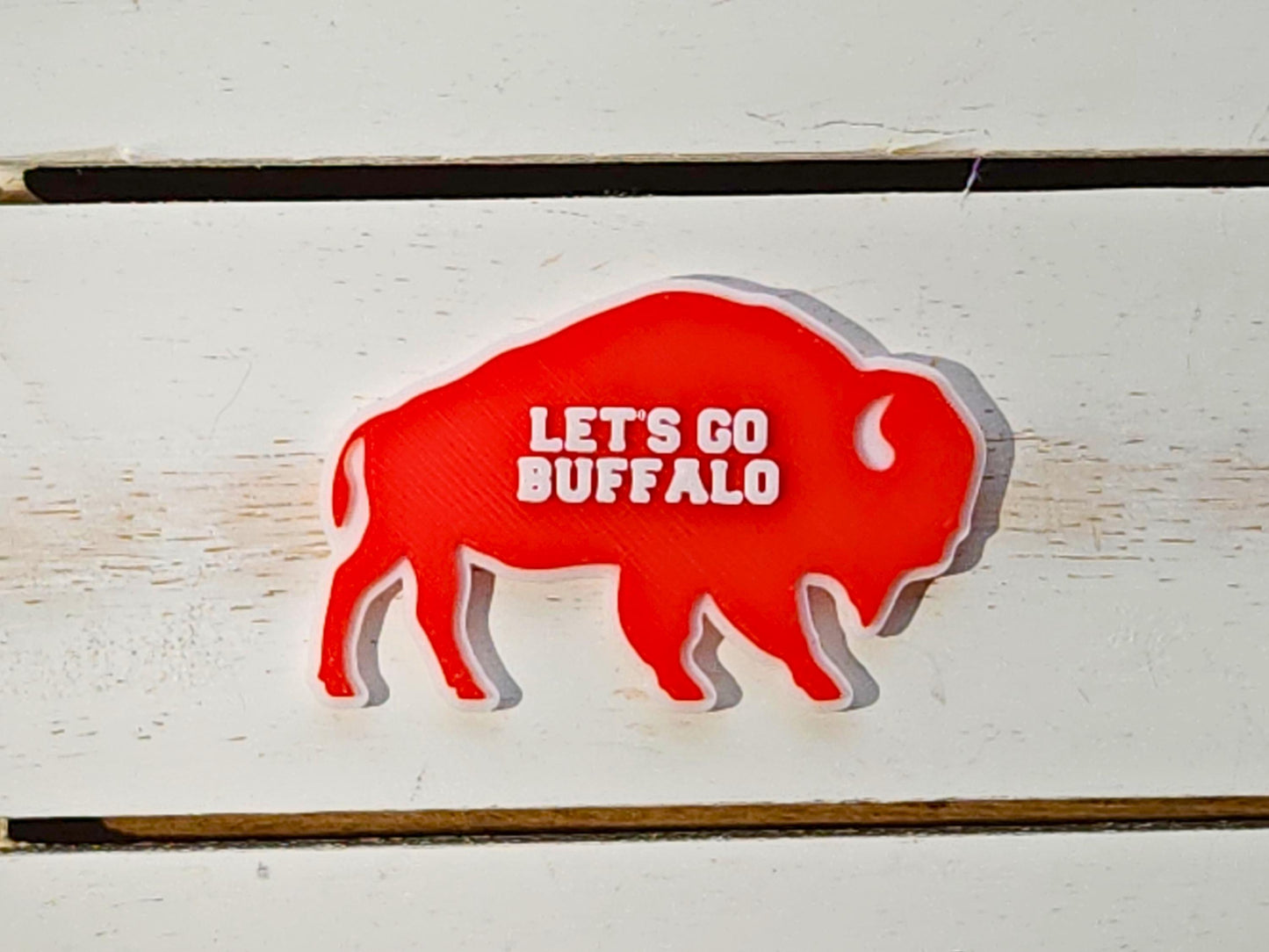 A single red Lets Go Buffalo magnets on a white wooden surface.