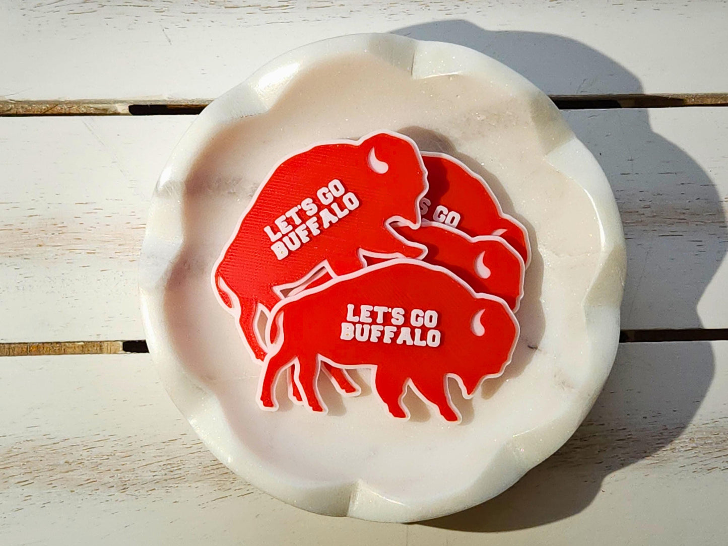 Pile of red Lets Go Buffalo magnets stacked in a white bowl on a wooden surface.