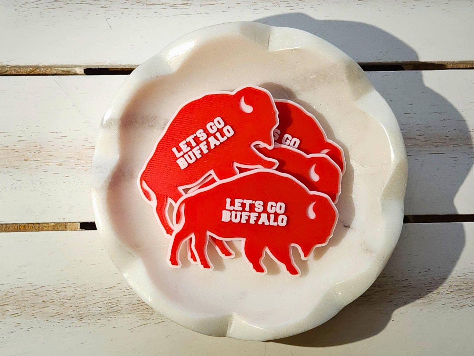Pile of red Lets Go Buffalo magnets stacked in a white bowl on a wooden surface.