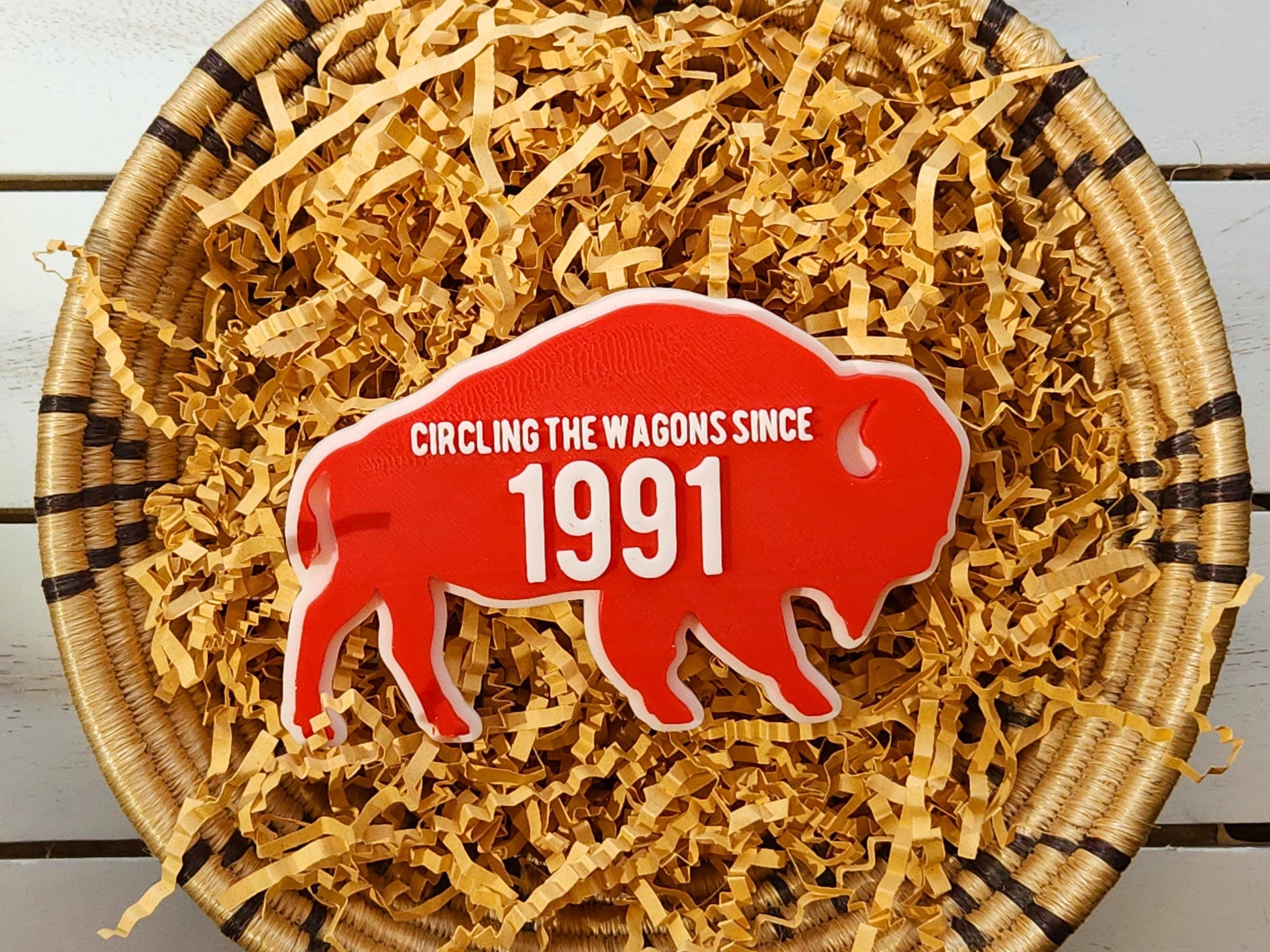 A red magnet for Buffalo Bills fans that says Circling the Wagons since 1991 that can be customized with any year. It is shown in a basket on a wooden background.