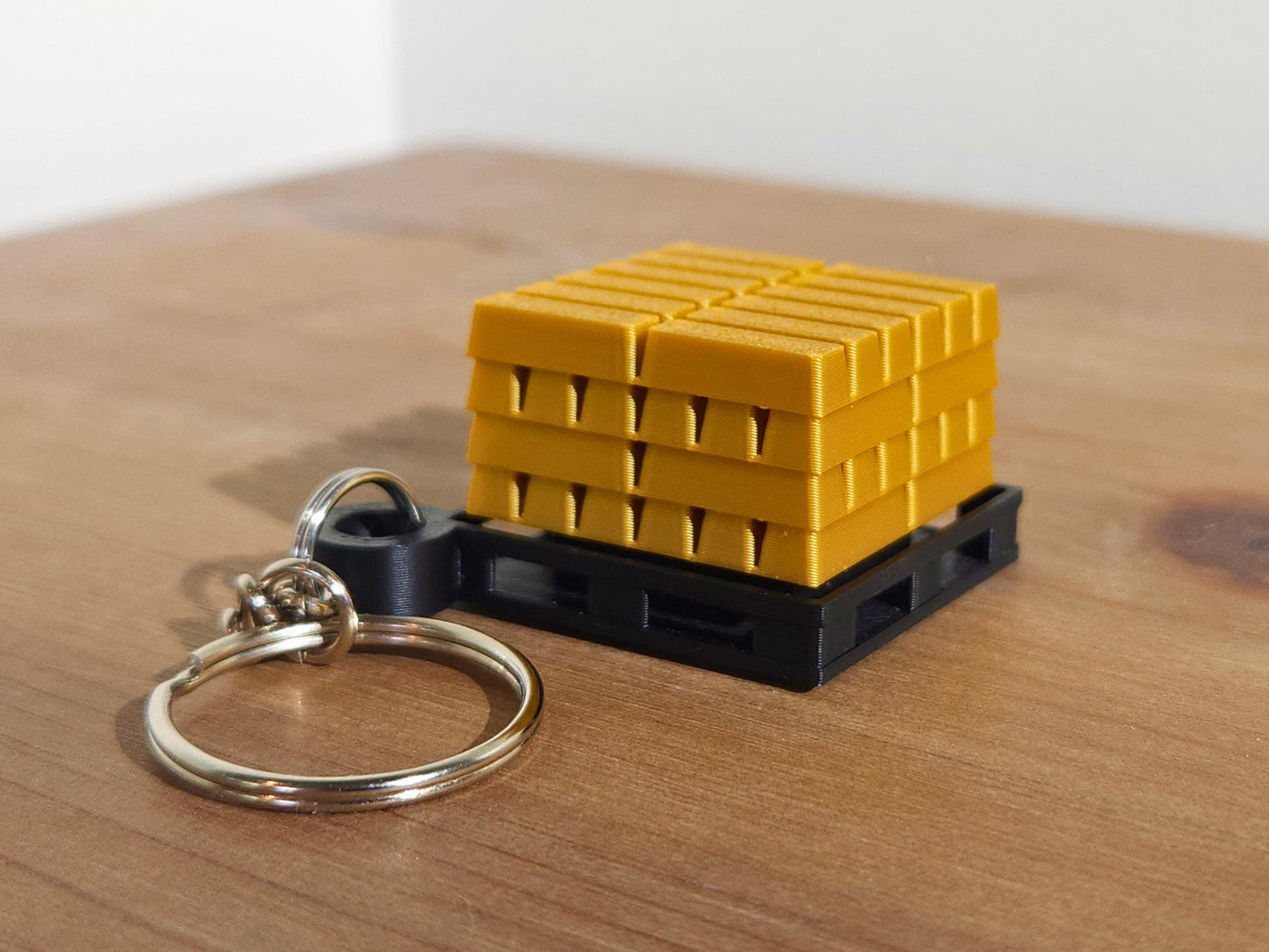 A close up picture of a single gold bar keychain from Fortnite, sitting on a table. The top has a mechanical clicker that can be used for anti-stress or fidgeting.