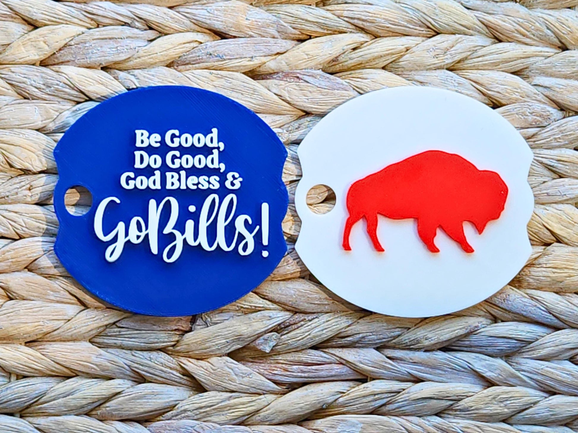 Two round Stanley cup toppers on a woven surface, one with red buffalo silhouette and the other with blue text reading Be Good, Do Good, God Bless & Go Bills!