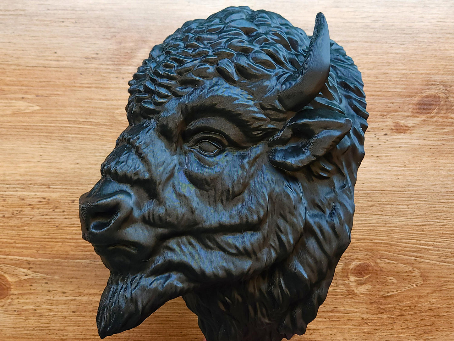 Left-side profile of a 3D printed buffalo wall head sculpture placed on a wooden surface, emphasizing the facial contours, horn curve, and fur texture.