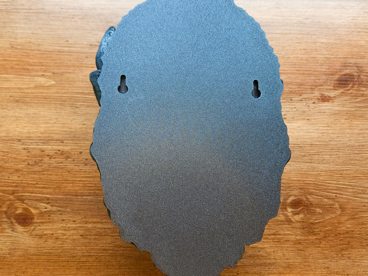 Rear view of the 3D printed buffalo wall head sculpture showing two built-in keyhole mounting slots for easy wall hanging, against a wood grain background.”