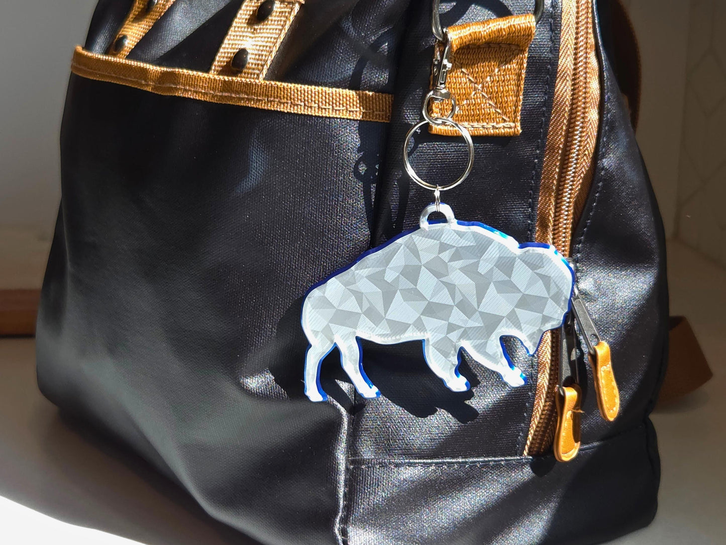 Buffalo football standing bison logo with geometric finish featured as a bag tag in silver with a blue backing.