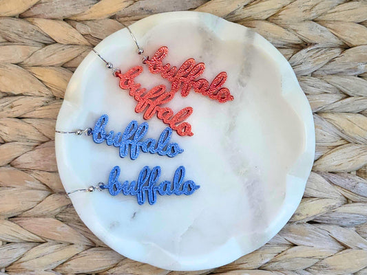 Two pairs of “buffalo” earrings, one red and one blue, styled together on a marble dish – ideal for mixing and matching team colors.