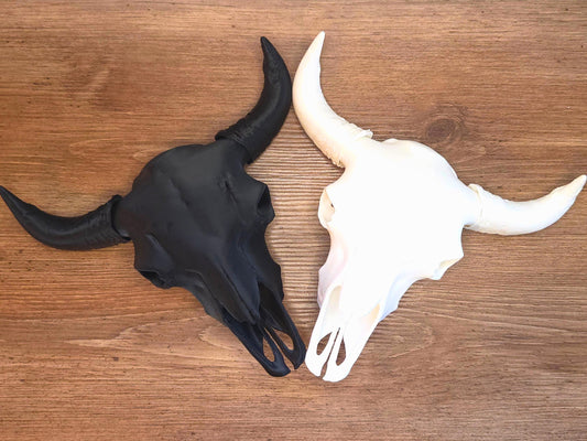 A black and white 3d printed bison skull are positioned next to each other on a wooden table.