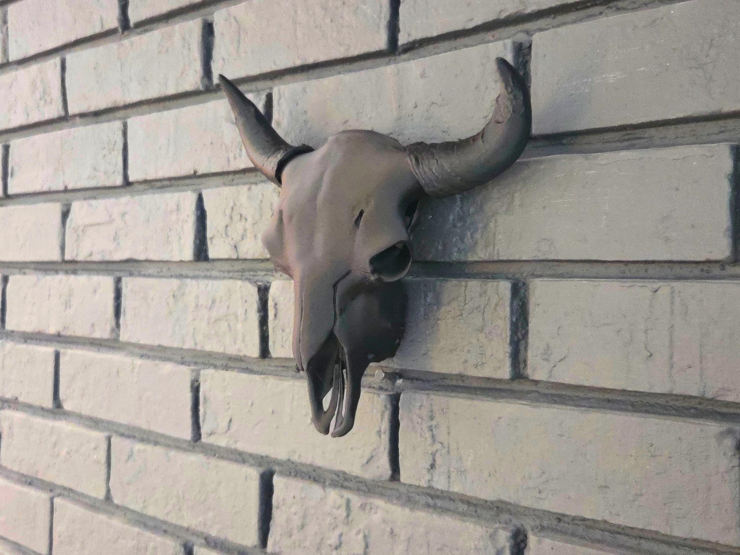 A black bison skull is hung on a black brick wall, showcasing ornate details.