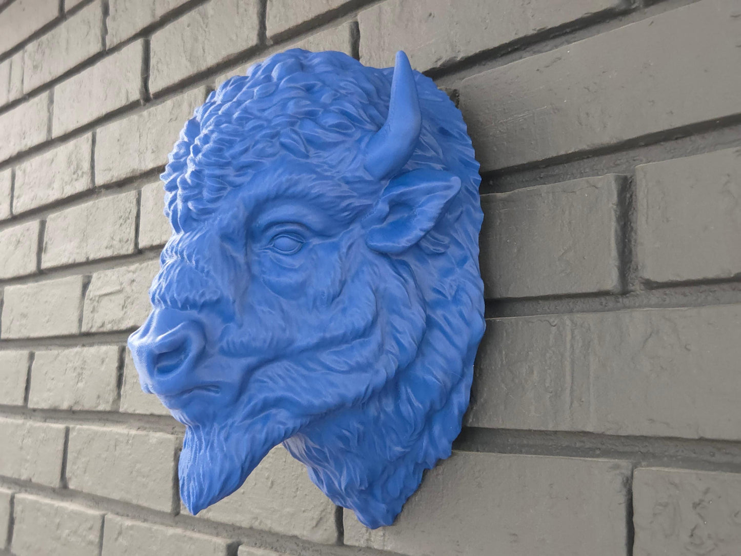 Blue and red bison head mounted on a black brick background highlighting ease of hanging and extreme detail.