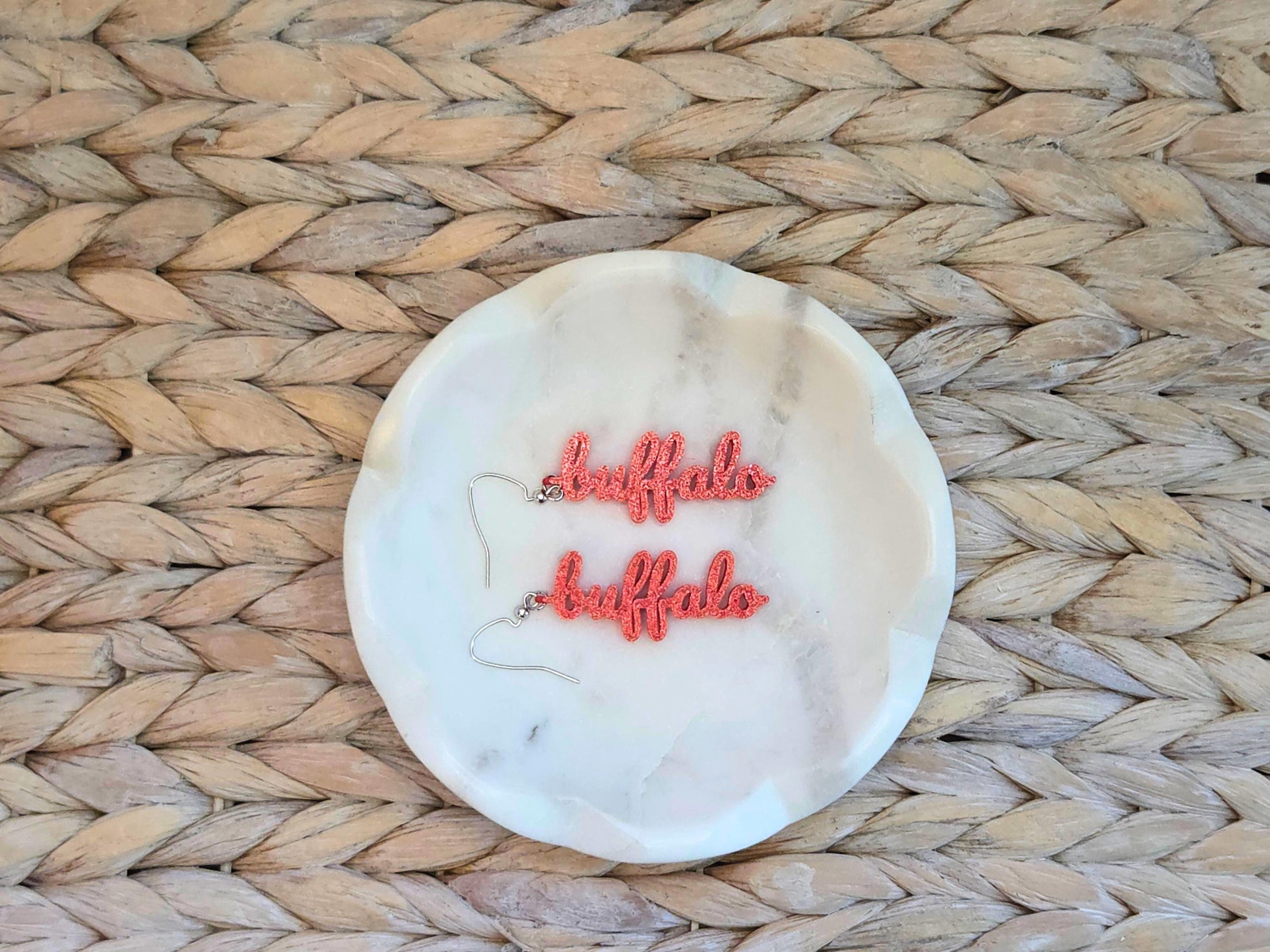 Red 3D printed “buffalo” earrings on a round marble display tray, ideal statement jewelry for Buffalo football fans.