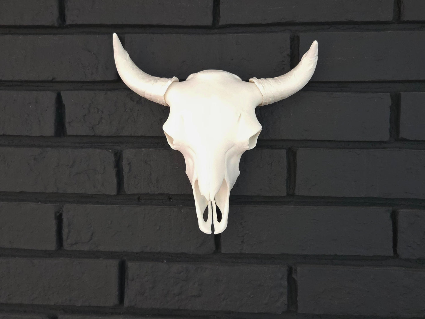 A white bison skull is hung on a black brick wall, showcasing ornate details.