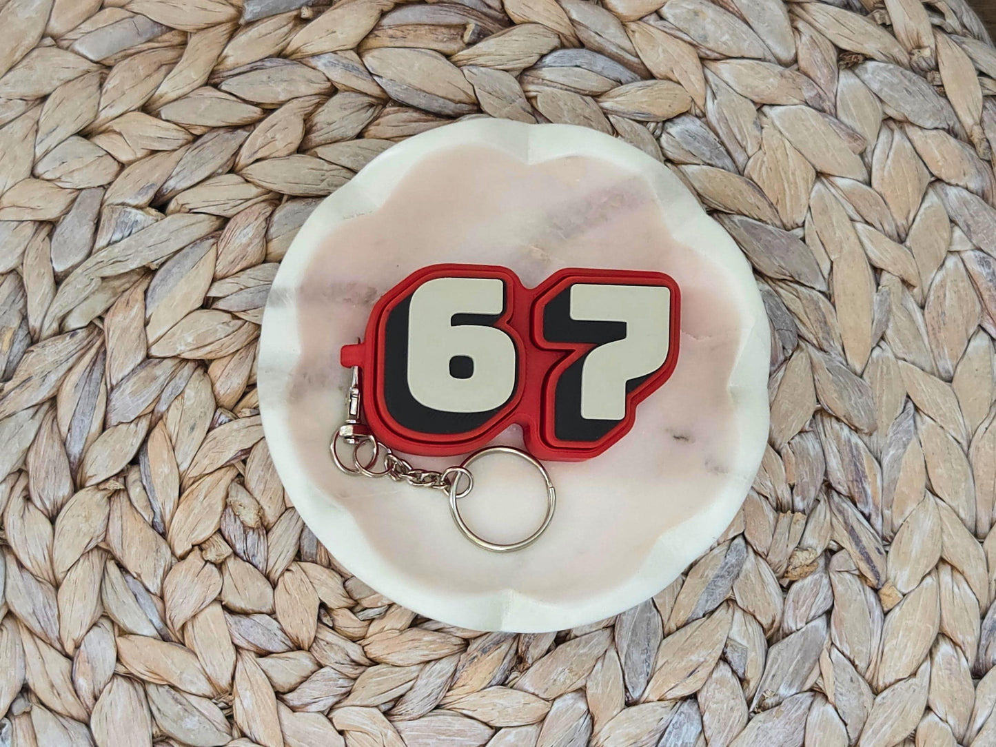 Picture of a red and tan fidget clicker keychain featuring the viral 67 meme in a dish on a woven surface.