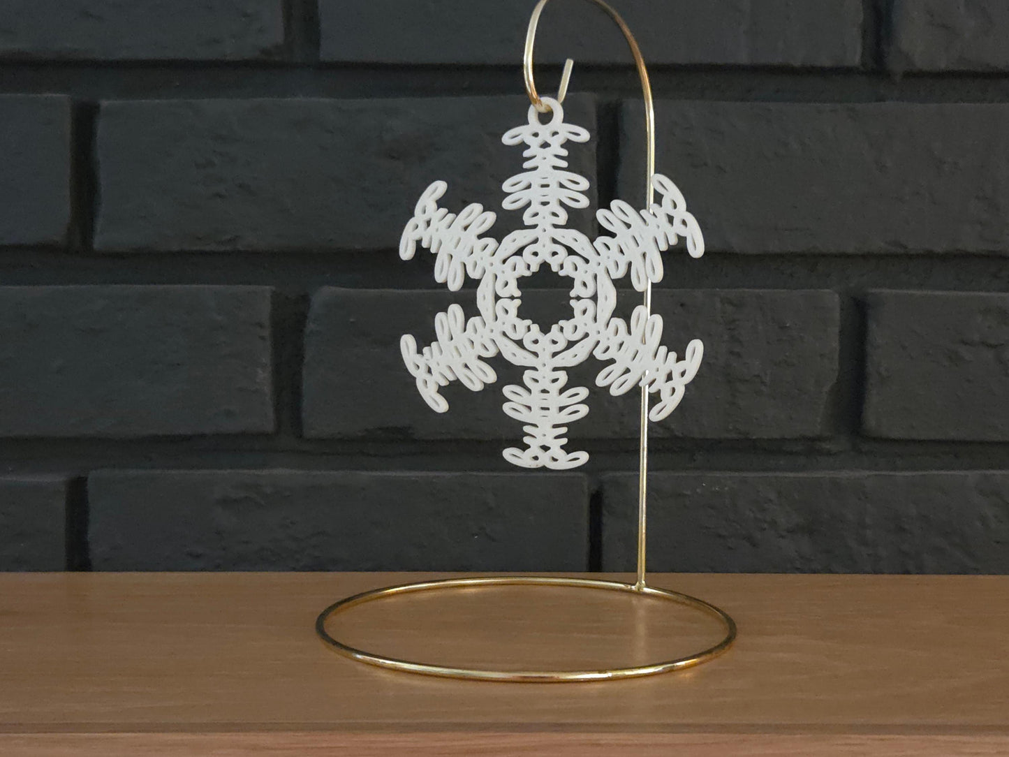 White snowflake christmas ornament that spells the word "Buffalo" hanging on a gold display hook in front of a black brick background.