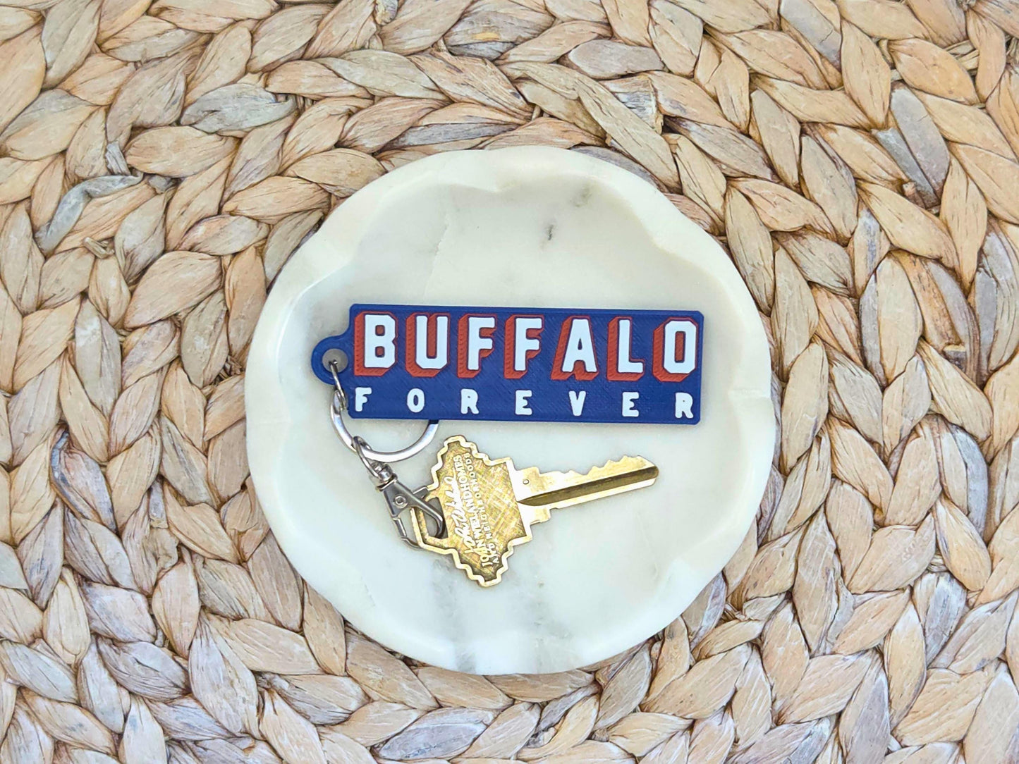 Buffalo Forever keychain is displayed in a white dish on a woven background. A key is shown for size.