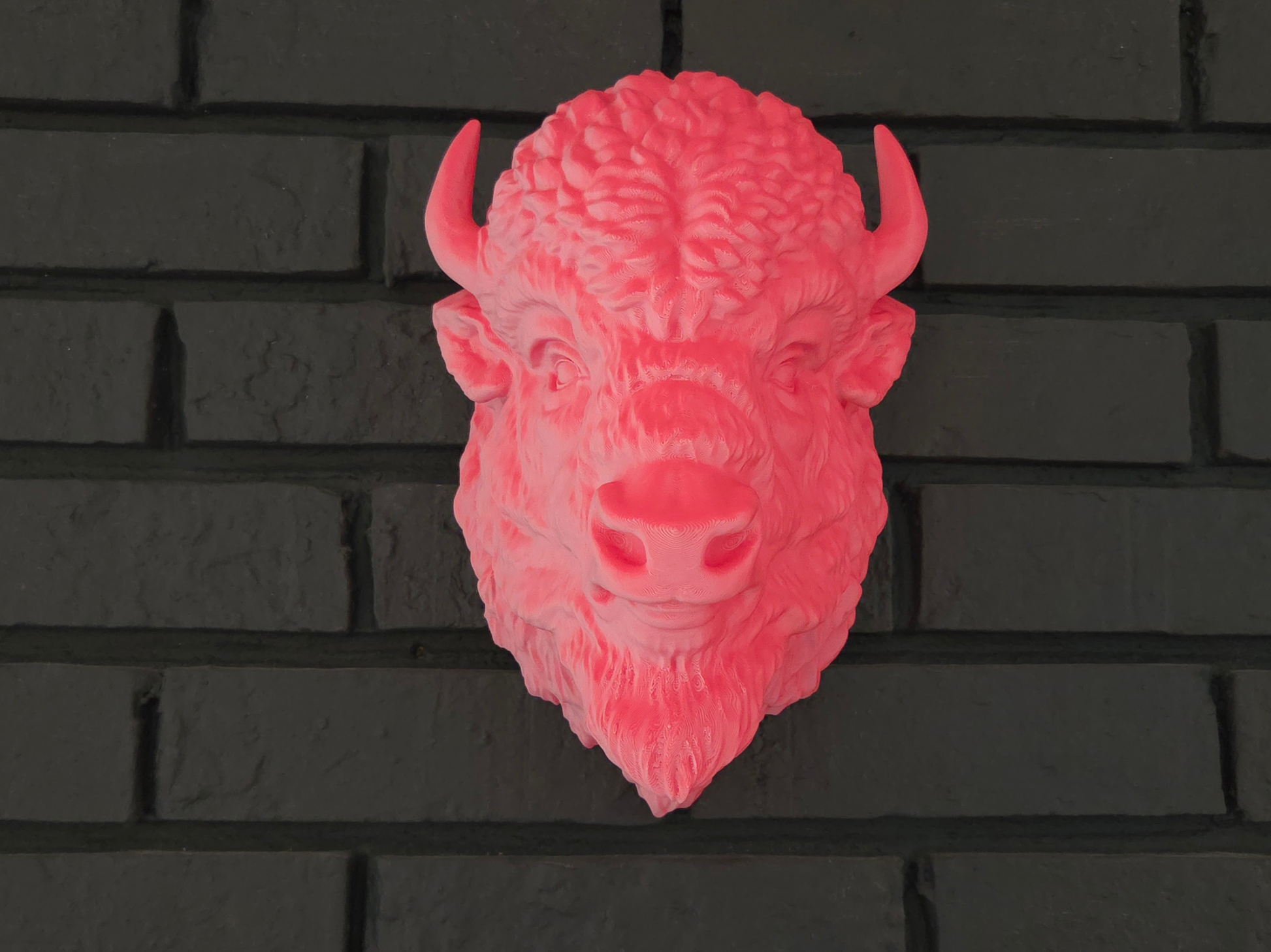 Pink buffalo head wall decoration on a black brick wall