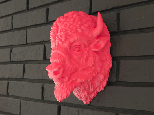 Pink bison head sculpture on a dark brick wall