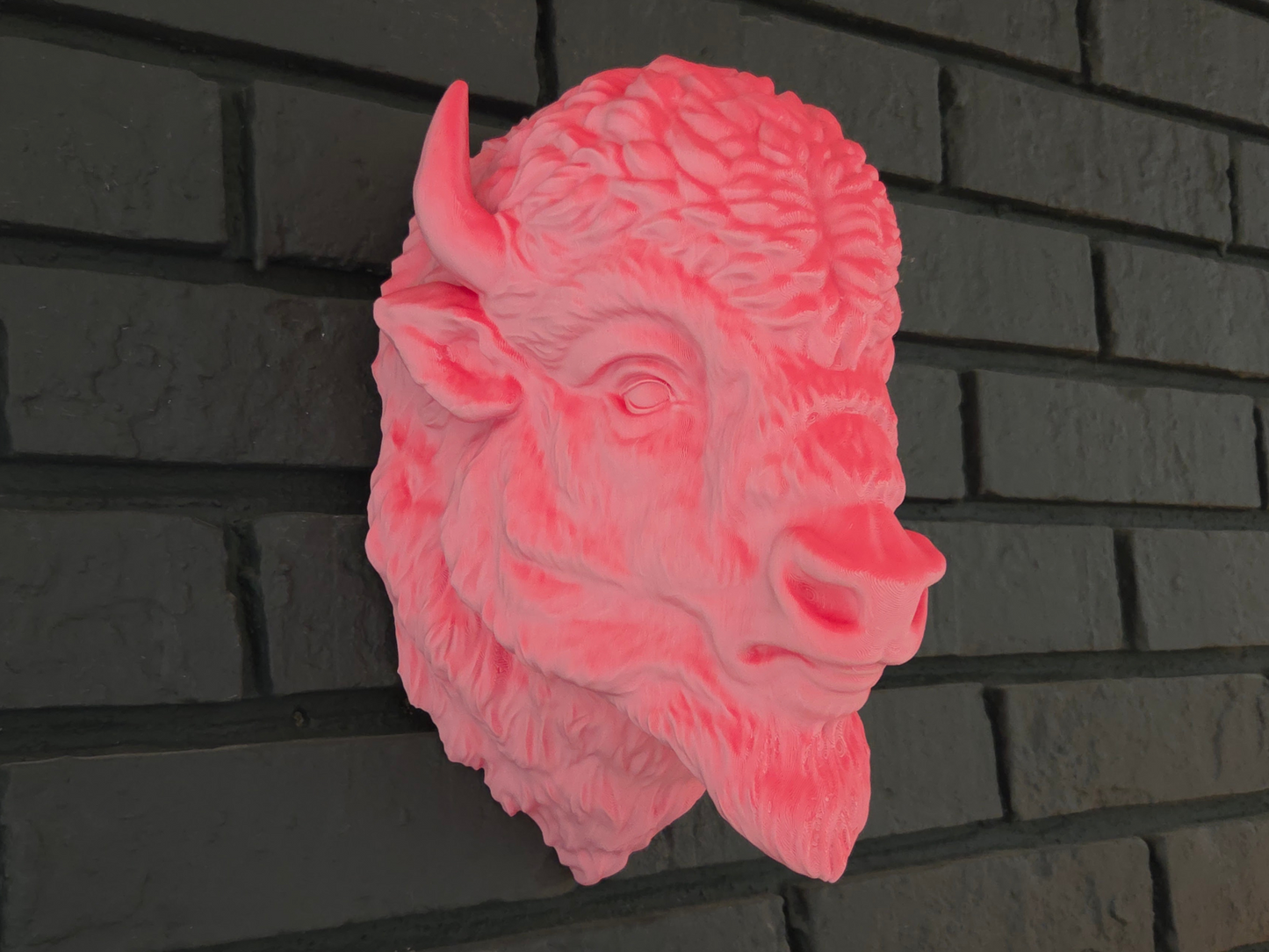 Pink buffalo head wall decoration on a dark brick wall