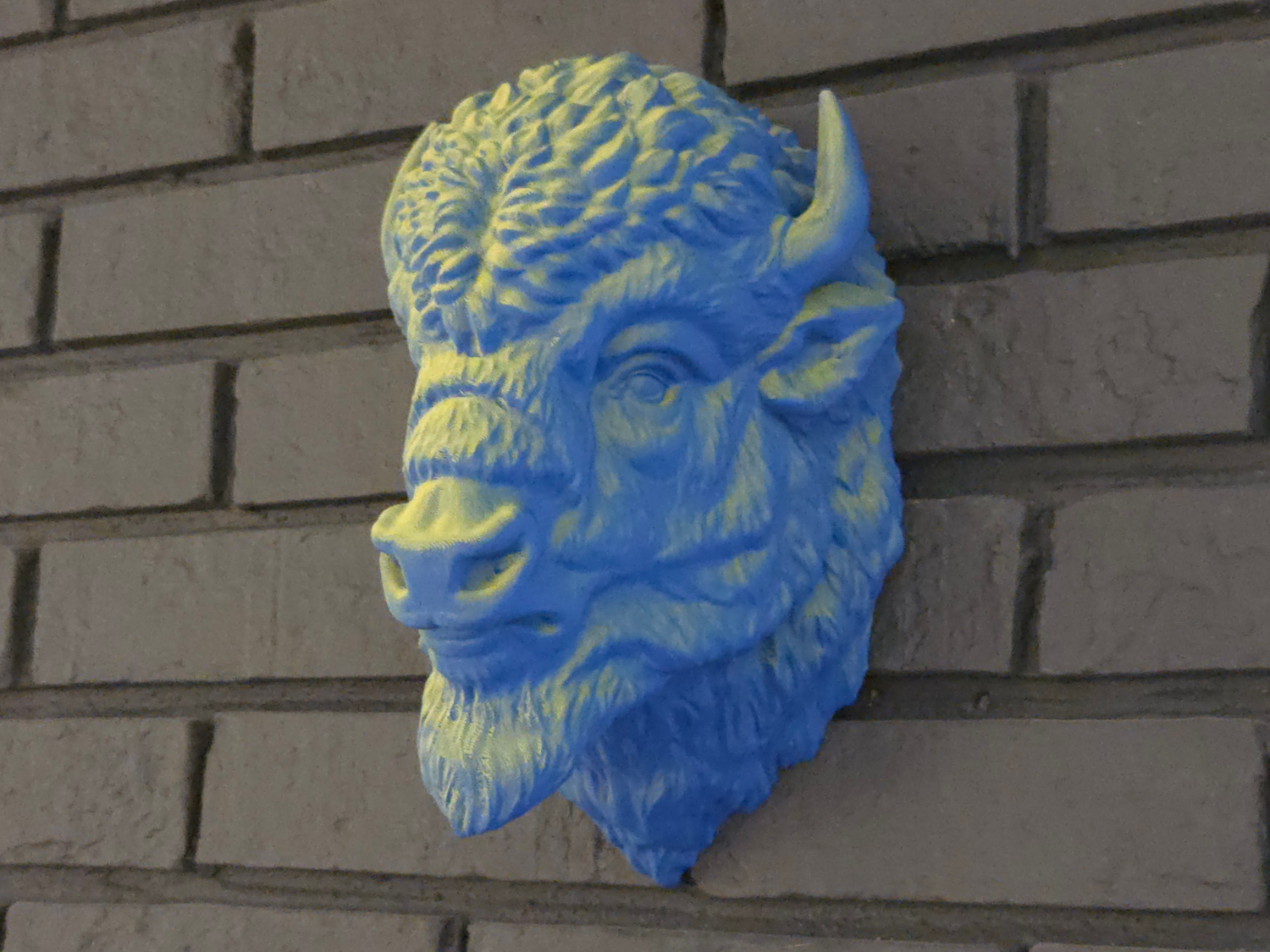 Blue and yellow buffalo head sculpture on a brick wall
