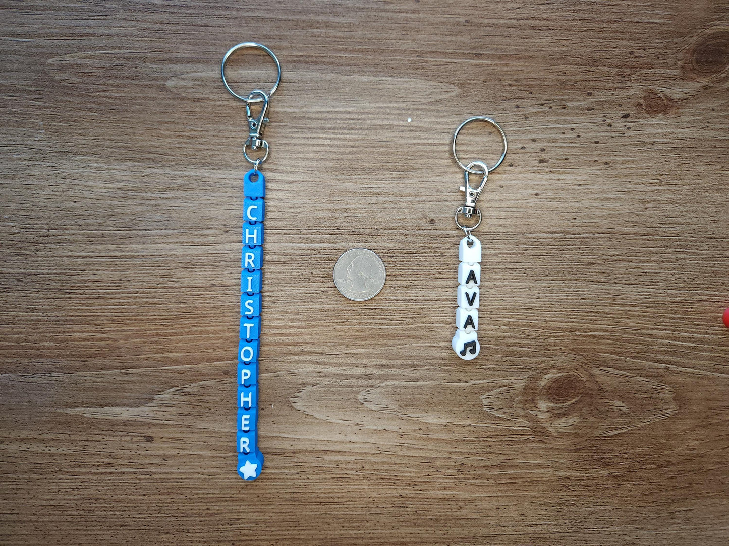 A side-by-side comparison of a long blue &quot;CHRISTOPHER&quot; keychain and a short white &quot;AVA&quot; keychain next to a coin for scale. Shows size options for personalized keychains.