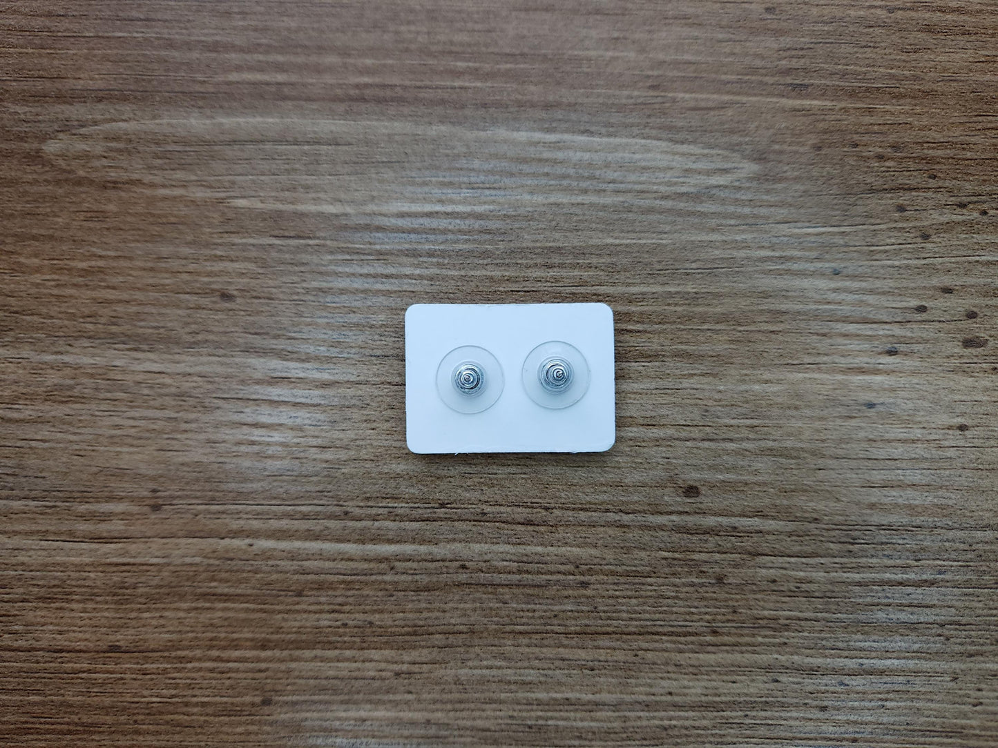 Close-up of the backs of heart-shaped stud earrings on a white display card, showcasing their secure design against a wooden surface.