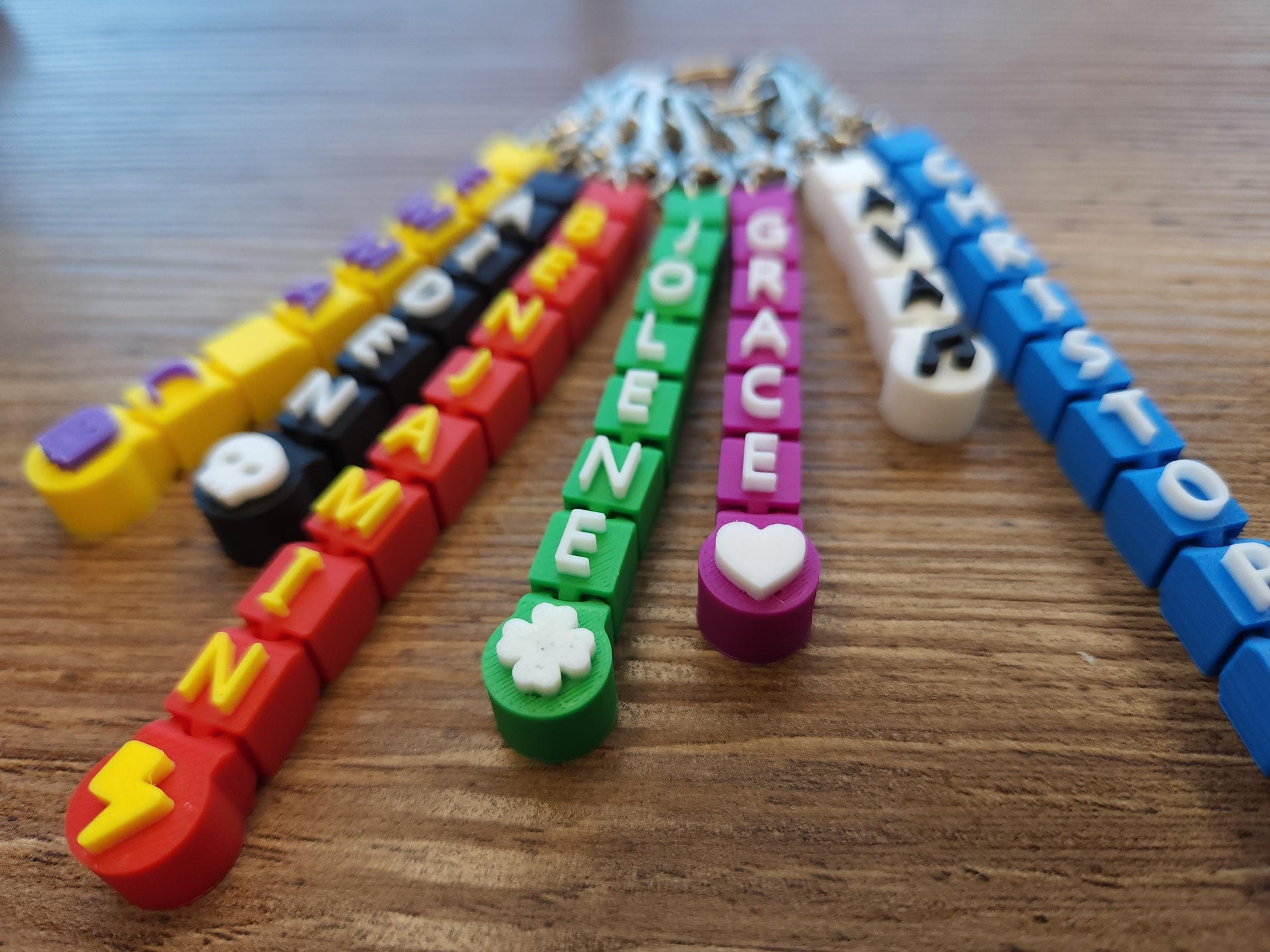 A colorful fan display of personalized keychains with names like &quot;EMMA&quot; and &quot;CHRISTOPHER,&quot; featuring fun symbols like stars and lightning bolts.