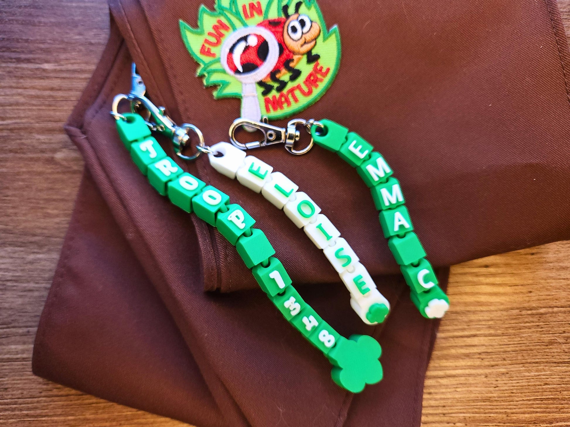 Three green and white keychains displayed on a brownie sash.