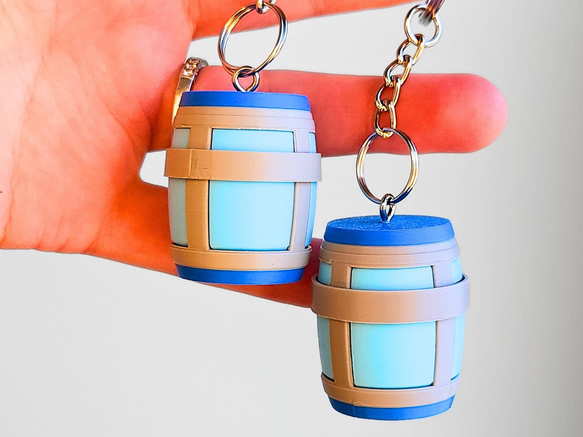 A close up picture of two Chug Jug keychains from Fortnite, hanging from a hand. The top of each clicks and can be used an anti-stress fidget toy.