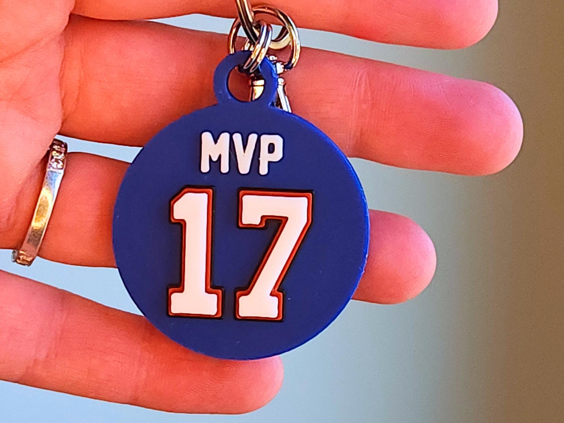 A blue keychain featuring the number 17 and phrase MVP being held from a hand to show the size and to commemorate Josh Allen&#39;s 2024 MVP Season with the Buffalo Bills.