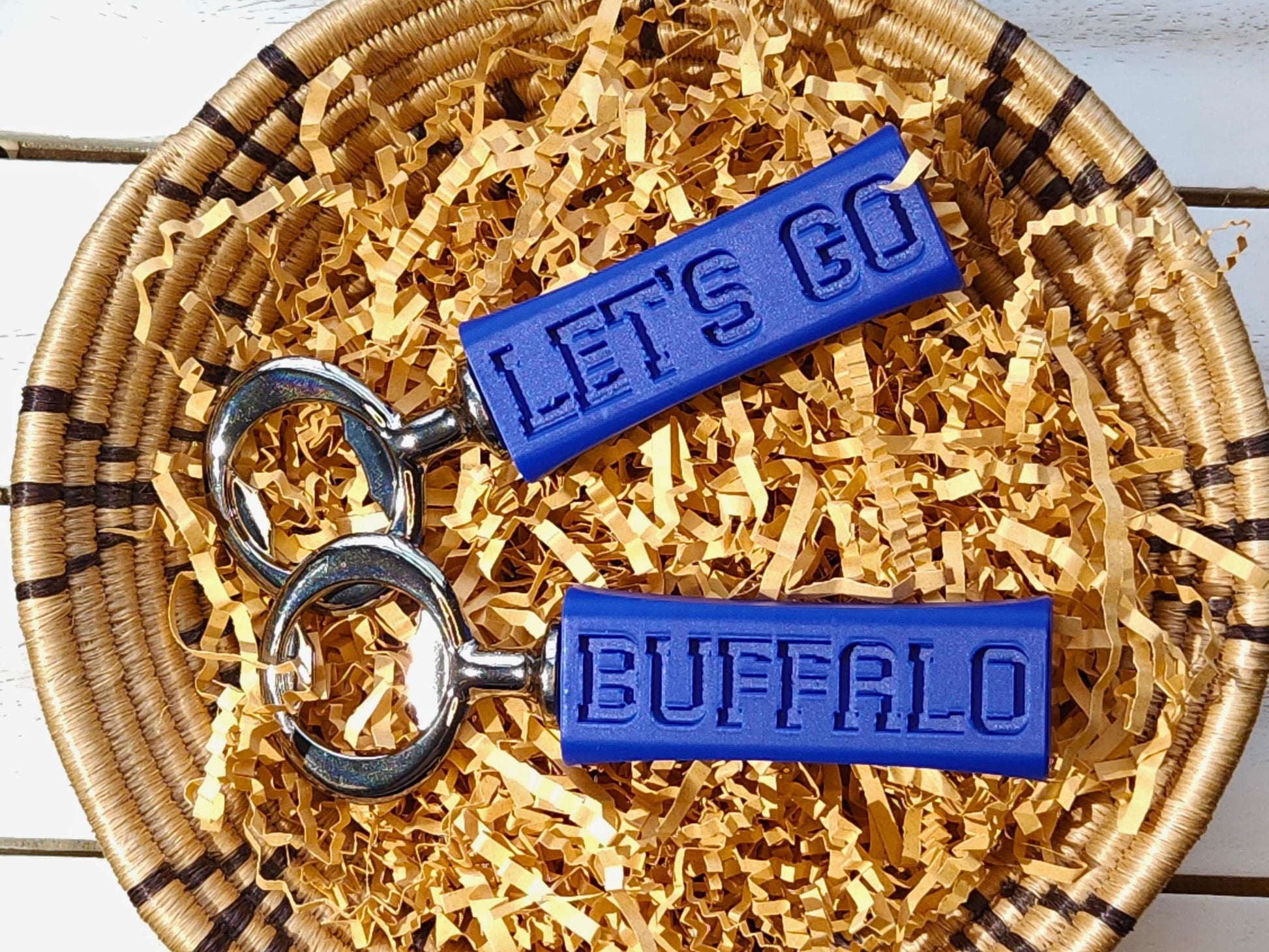 Two buffalo bills bottle openers side by side in a basket, showcasing their compact and stylish design. They say Let&#39;s Go Buffalo in embossed letters on the side of them.