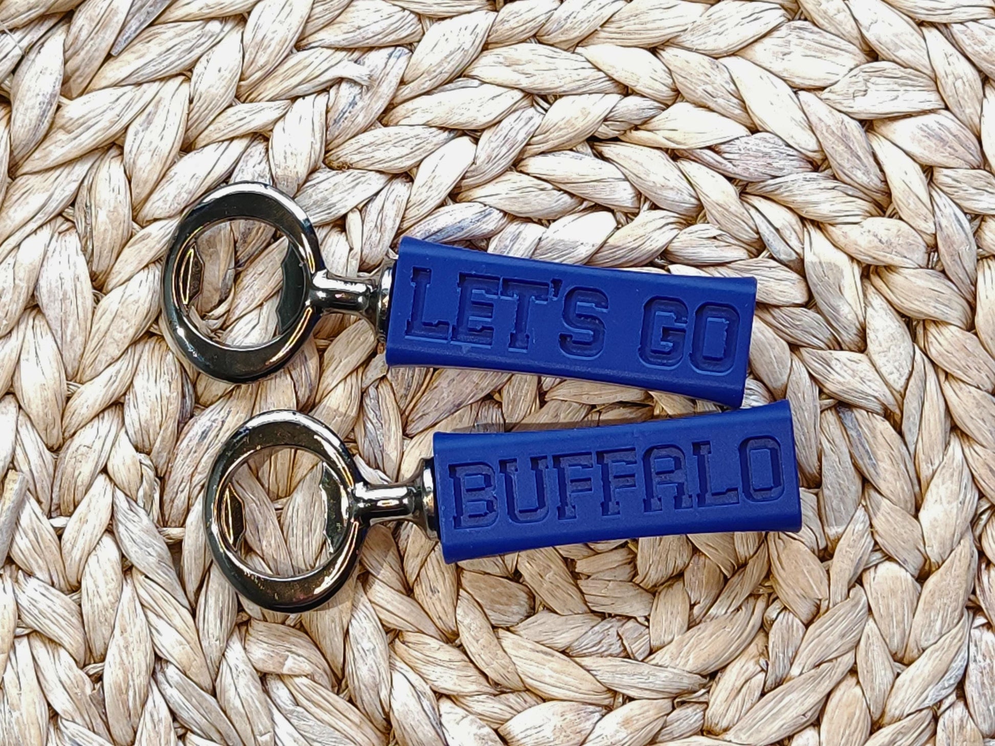 Two buffalo bills bottle openers side by side on a woven surface, showcasing their compact and stylish design. they say let&#39;s go buffalo on them.