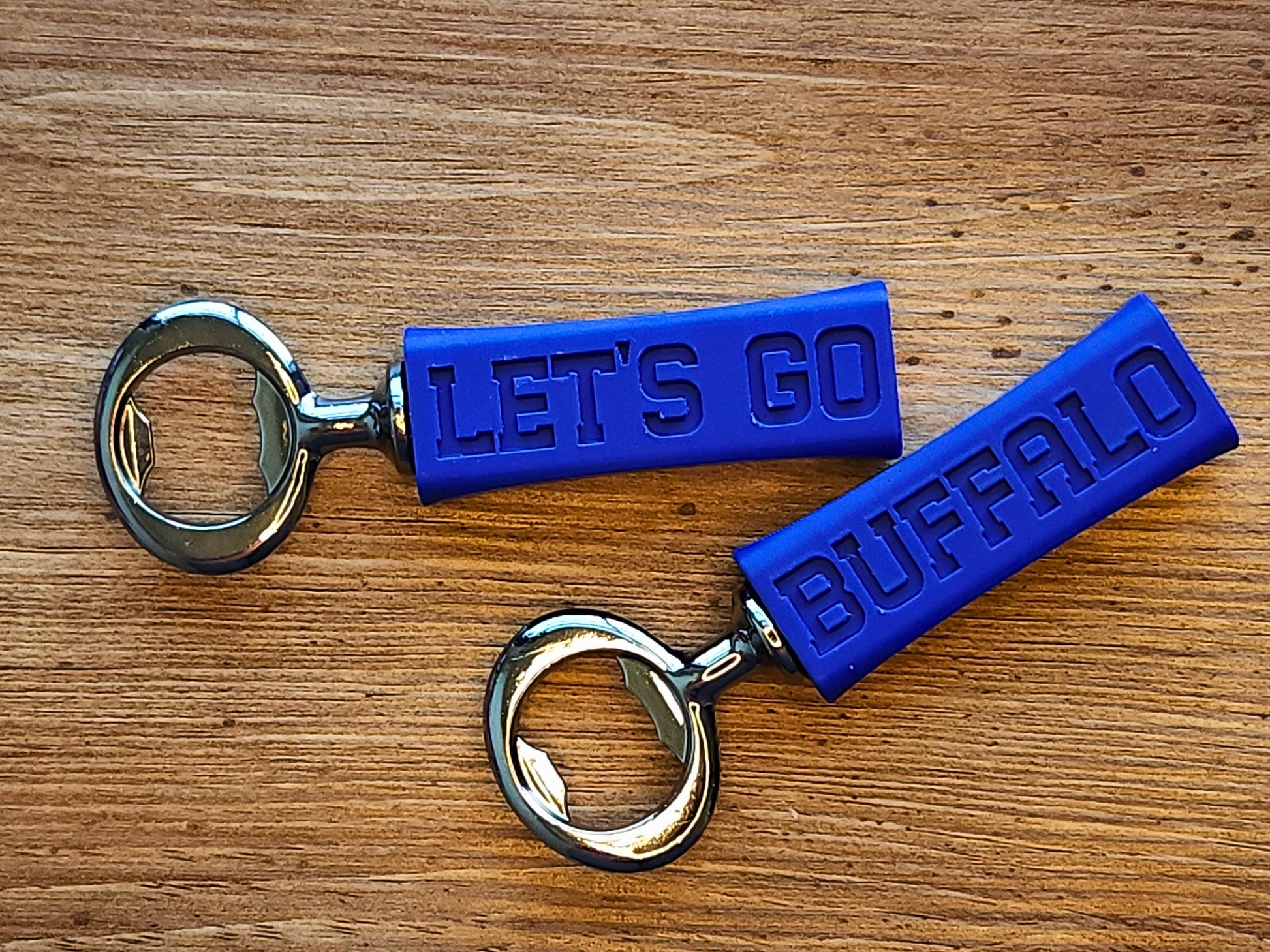 A pair of blue 3D-printed bottle openers with Let’s Go Buffalo embossed on them, placed in a woven basket on a wooden surface.