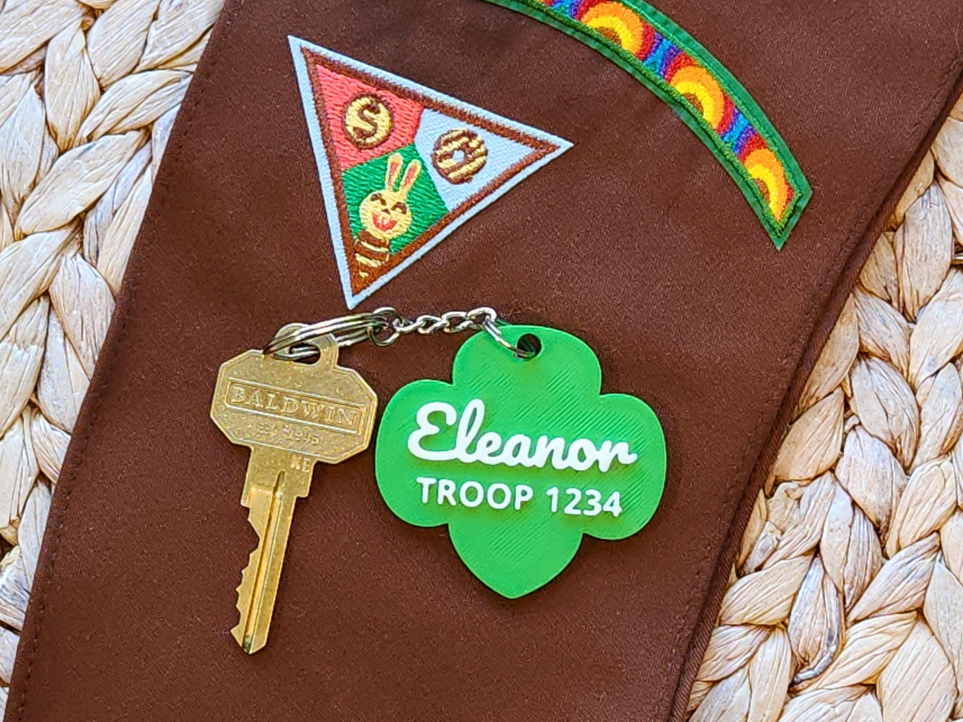 Custom Girl Scout Brownie keychain with name &quot;Eleanor&quot; and Troop 1234 in white lettering on a green trefoil, displayed on a Girl Scout Brownie sash with earned patches.
