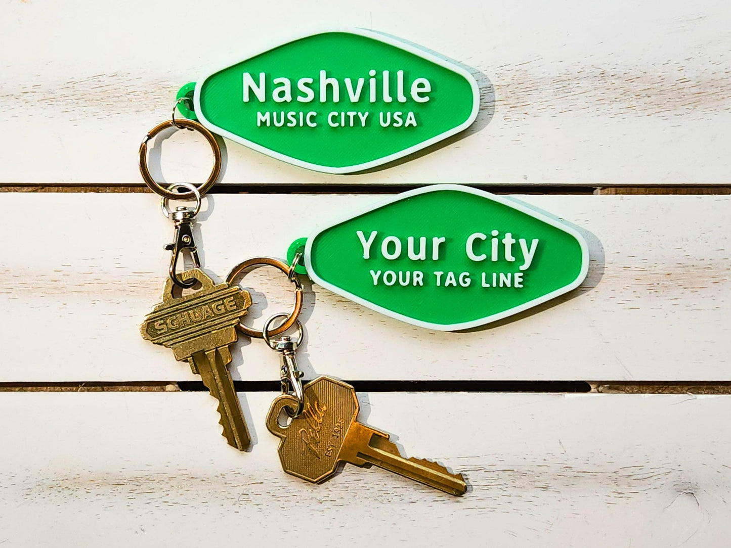 Nashville and custom hometown keychains side by side on a white wooden surface, both attached to keys.