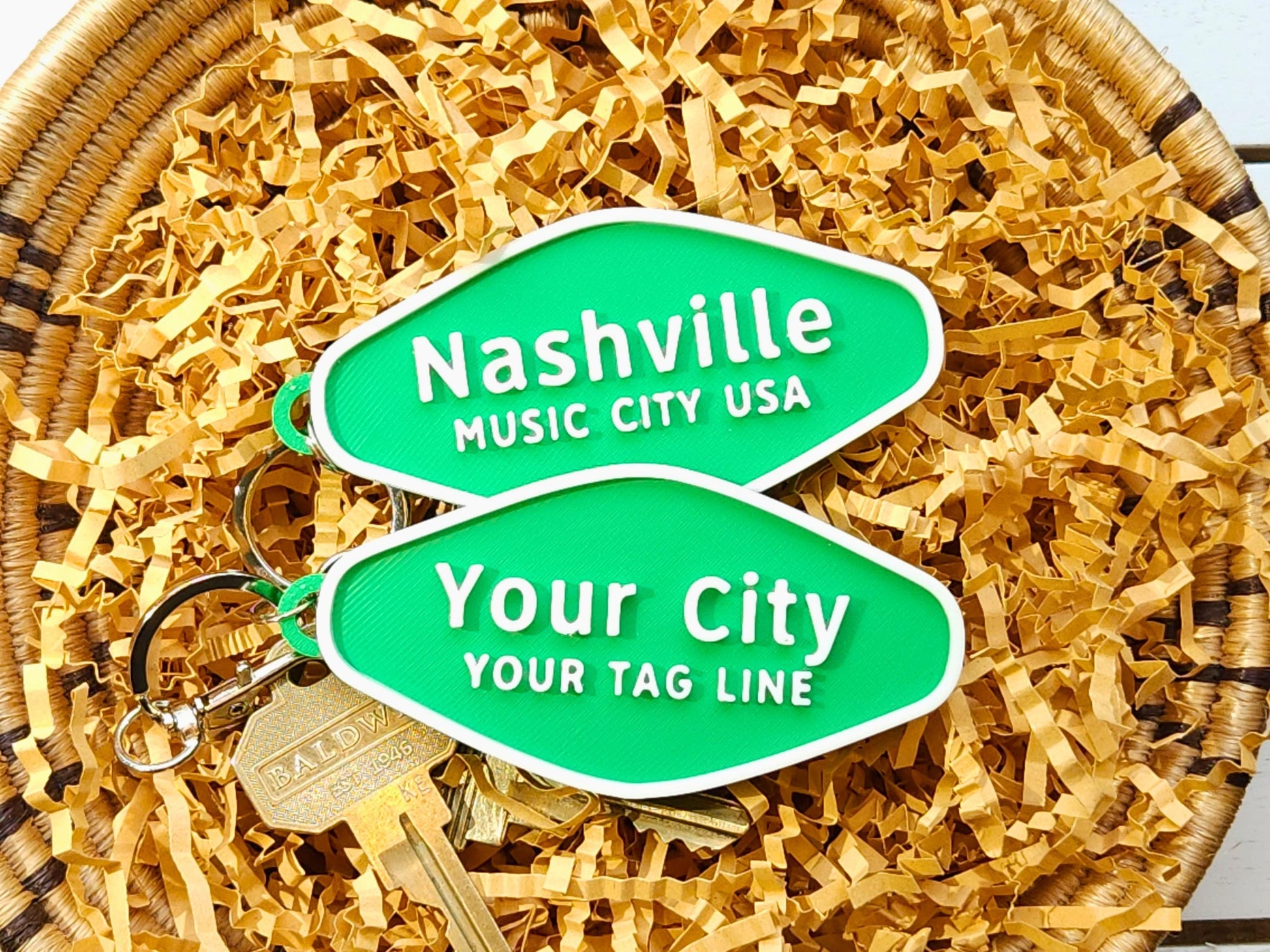 Two green street-sign-shaped keychains with white border and text – one says “Nashville, Music City USA” and the other is a customizable “Your City, Your Tag Line.” Set on shredded packing paper.