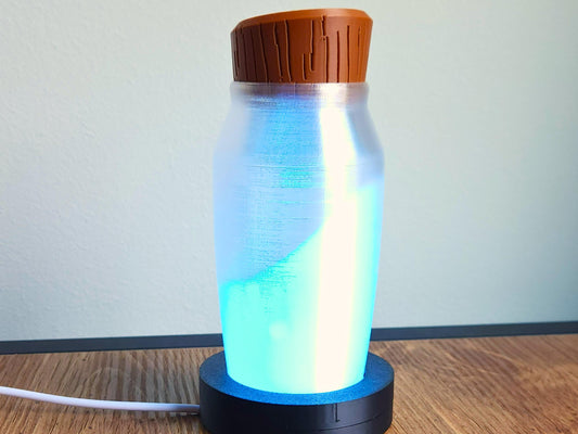 A glowing potion bottle lamp illuminated in blue light, sitting on its black circular base, with a white wall background.