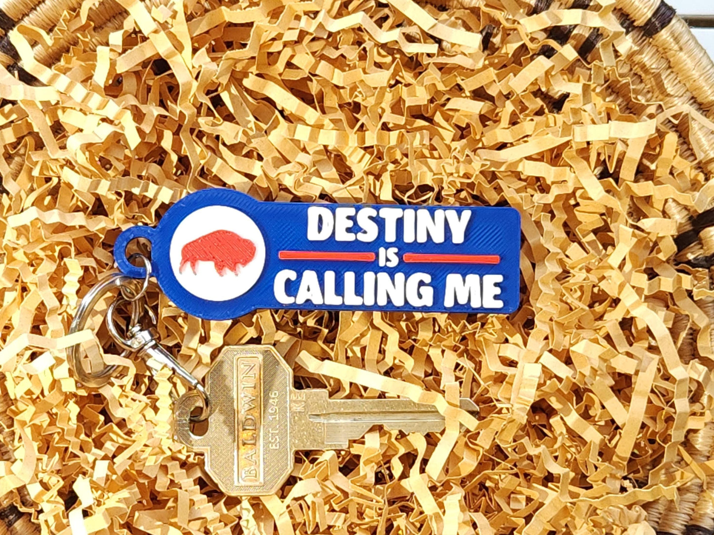 A blue keychain that says Destiny is Calling Me Go Bills displayed in a basket with keys.