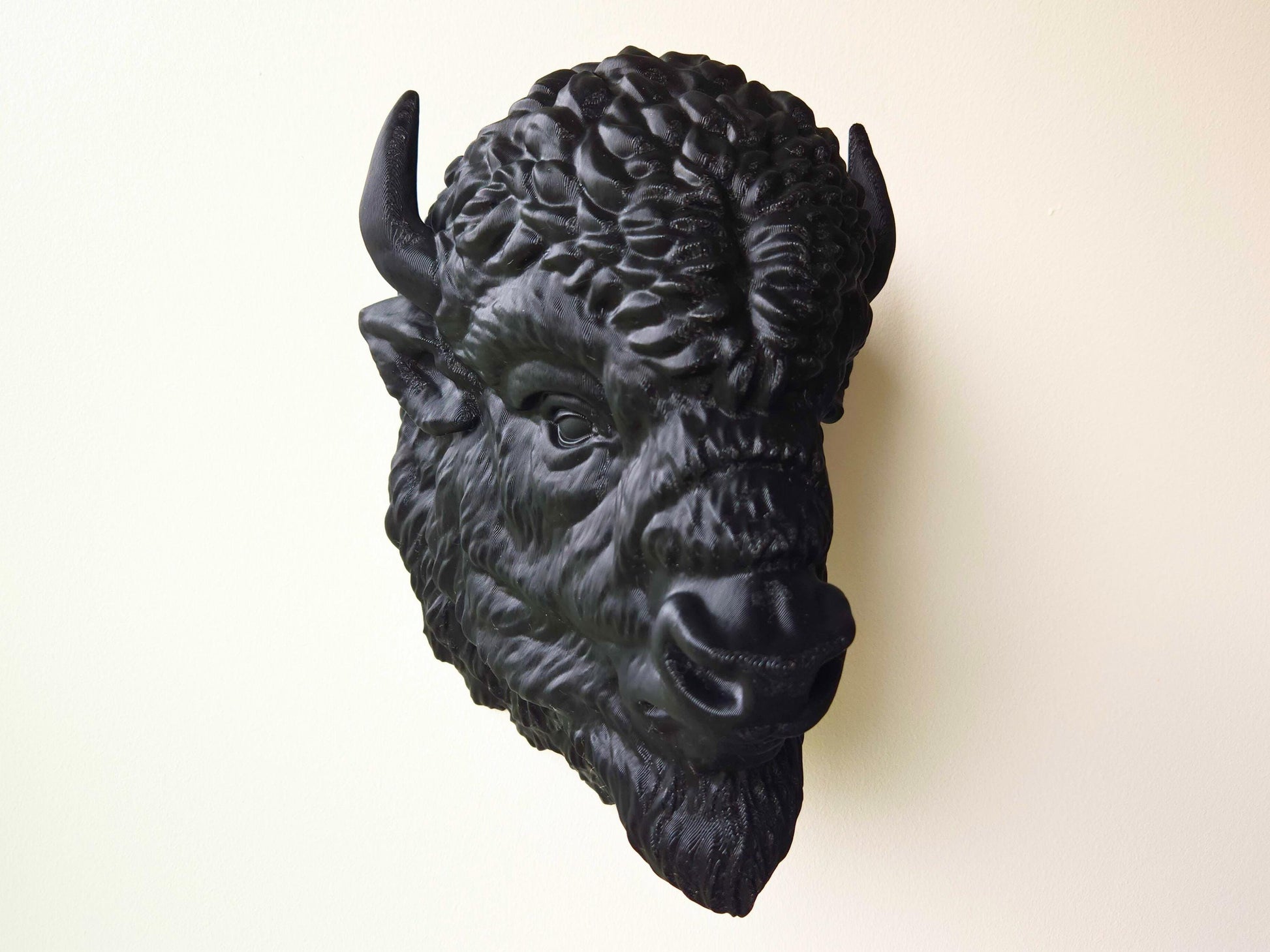 Angled view of a black buffalo wall head sculpture mounted on a light-colored wall, showing off its dimensional features and handcrafted detail.