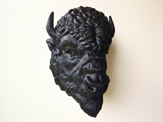 Angled view of a black buffalo wall head sculpture mounted on a light-colored wall, showing off its dimensional features and handcrafted detail.