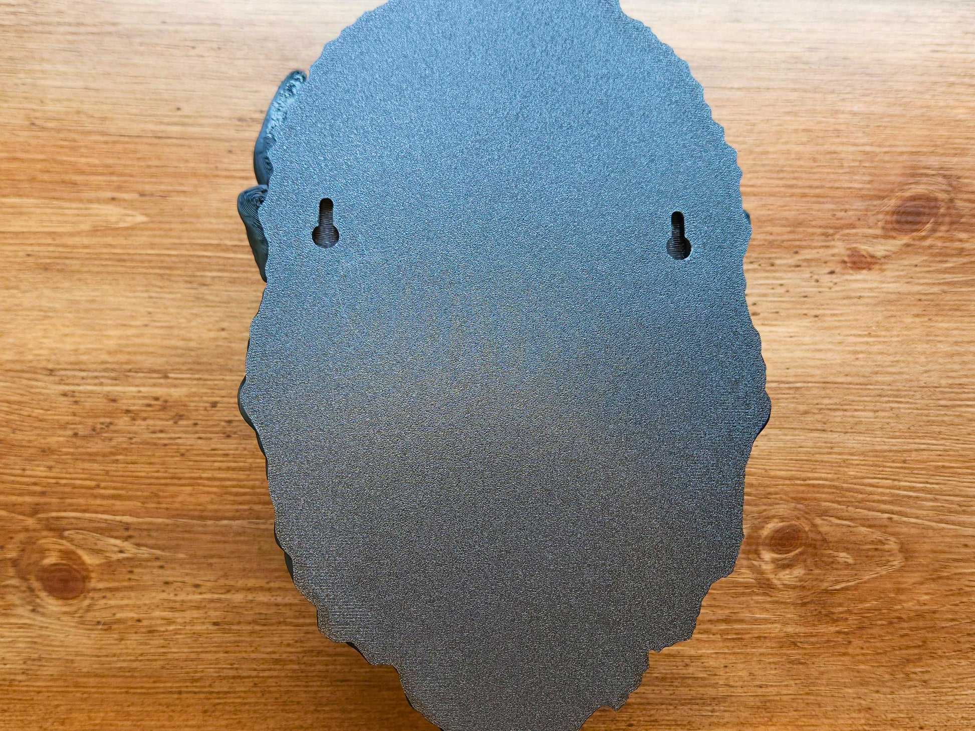 Rear view of the 3D printed buffalo wall head sculpture showing two built-in keyhole mounting slots for easy wall hanging, against a wood grain background.”