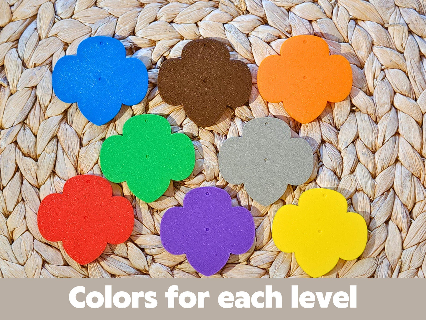 Girl Scout keychain color options for each level: blue, brown, orange, red, green, gray, purple, and yellow trefoil shapes displayed on woven mat with text &quot;Colors for each level.&quot;